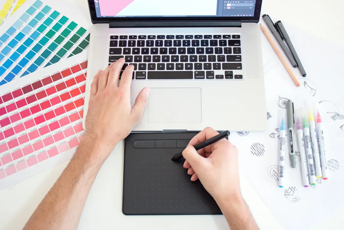 Designer choosing colours with a pen tablet beside a printed colour chart